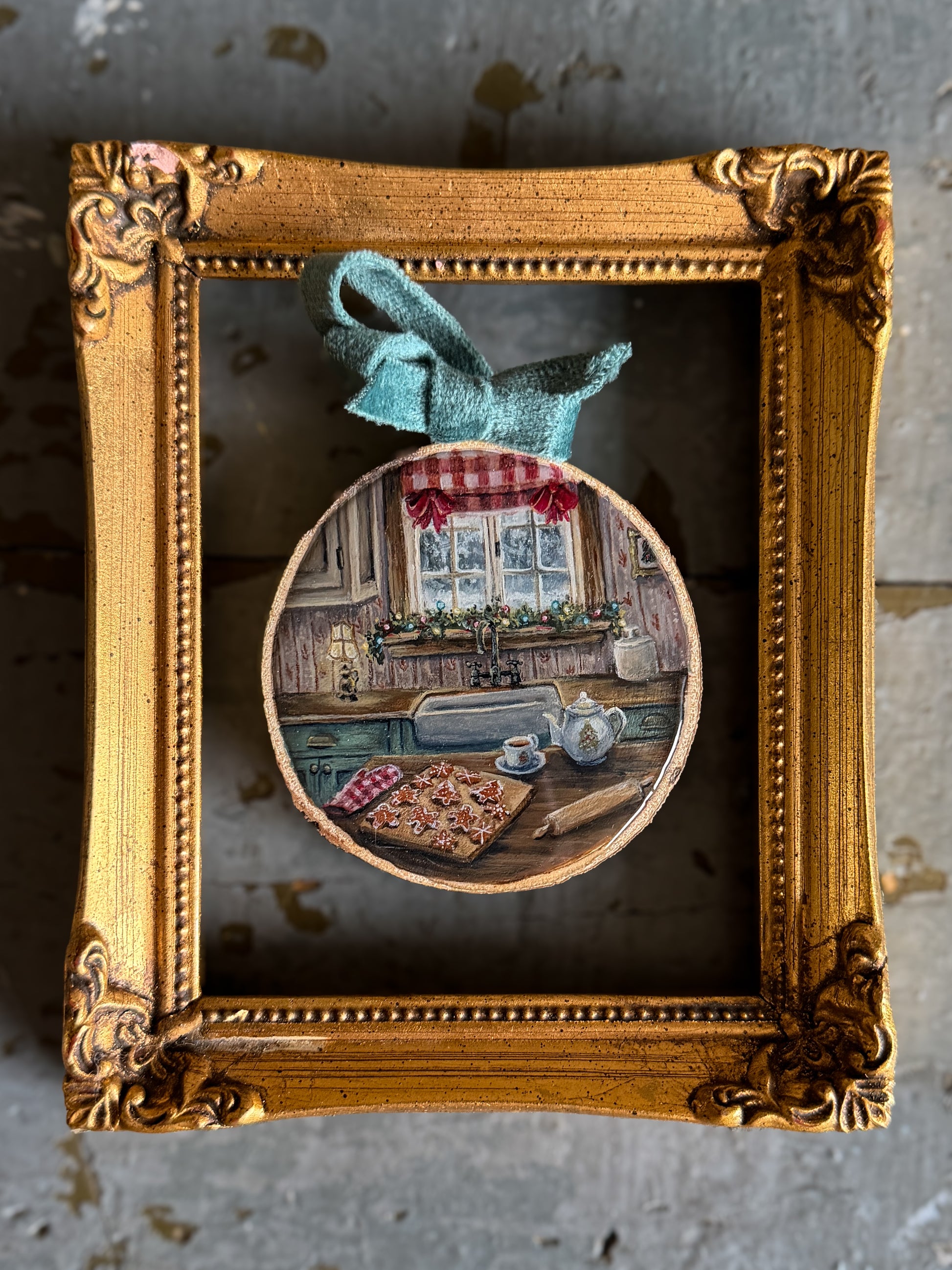 a hand-painted Christmas cookie scene on a wood slice with a blue velvet bow presented in an ornate gold frame